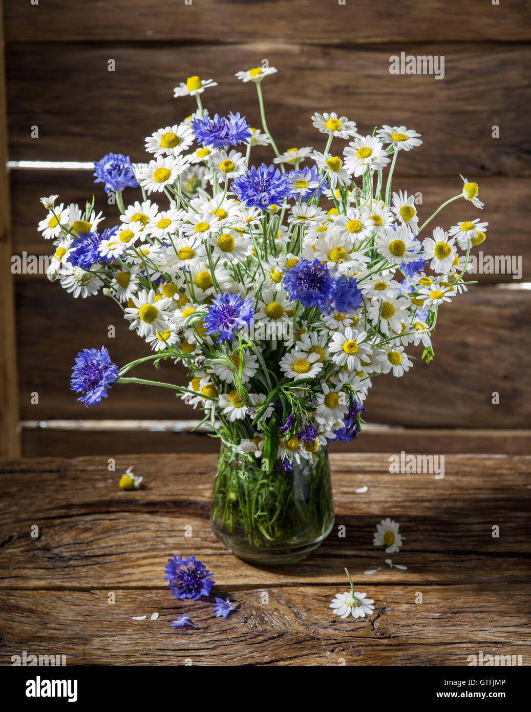 Bouquet of chamomiles and cornflowers in the vase on the wooden table. Stock Photo