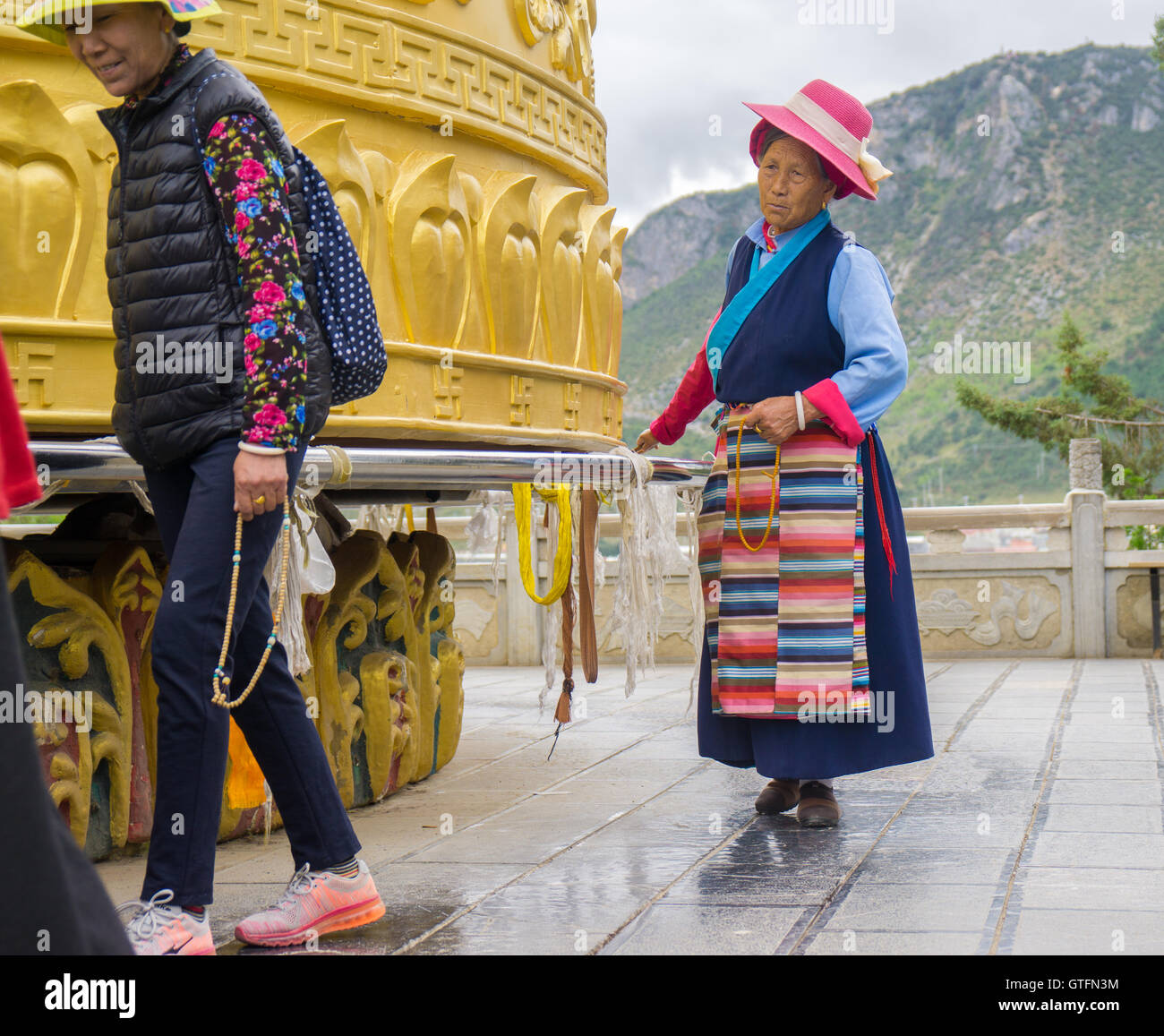 Old Chinese woman spinning the biggest prayer wheel in the world Stock Photo