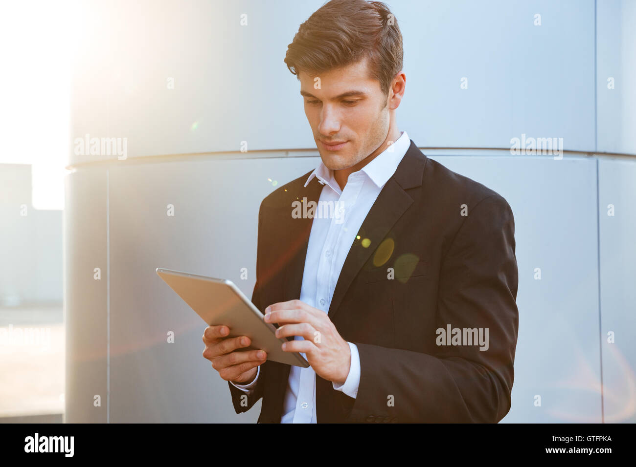 Attractive young serious businessman standing outdoors and using pc tablet Stock Photo