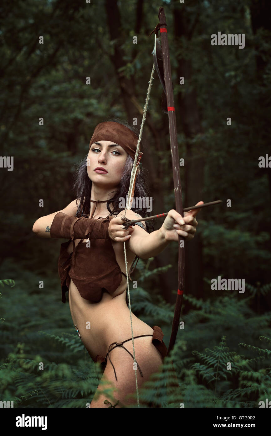 Beautiful huntress aiming with bow . Forest survival Stock Photo