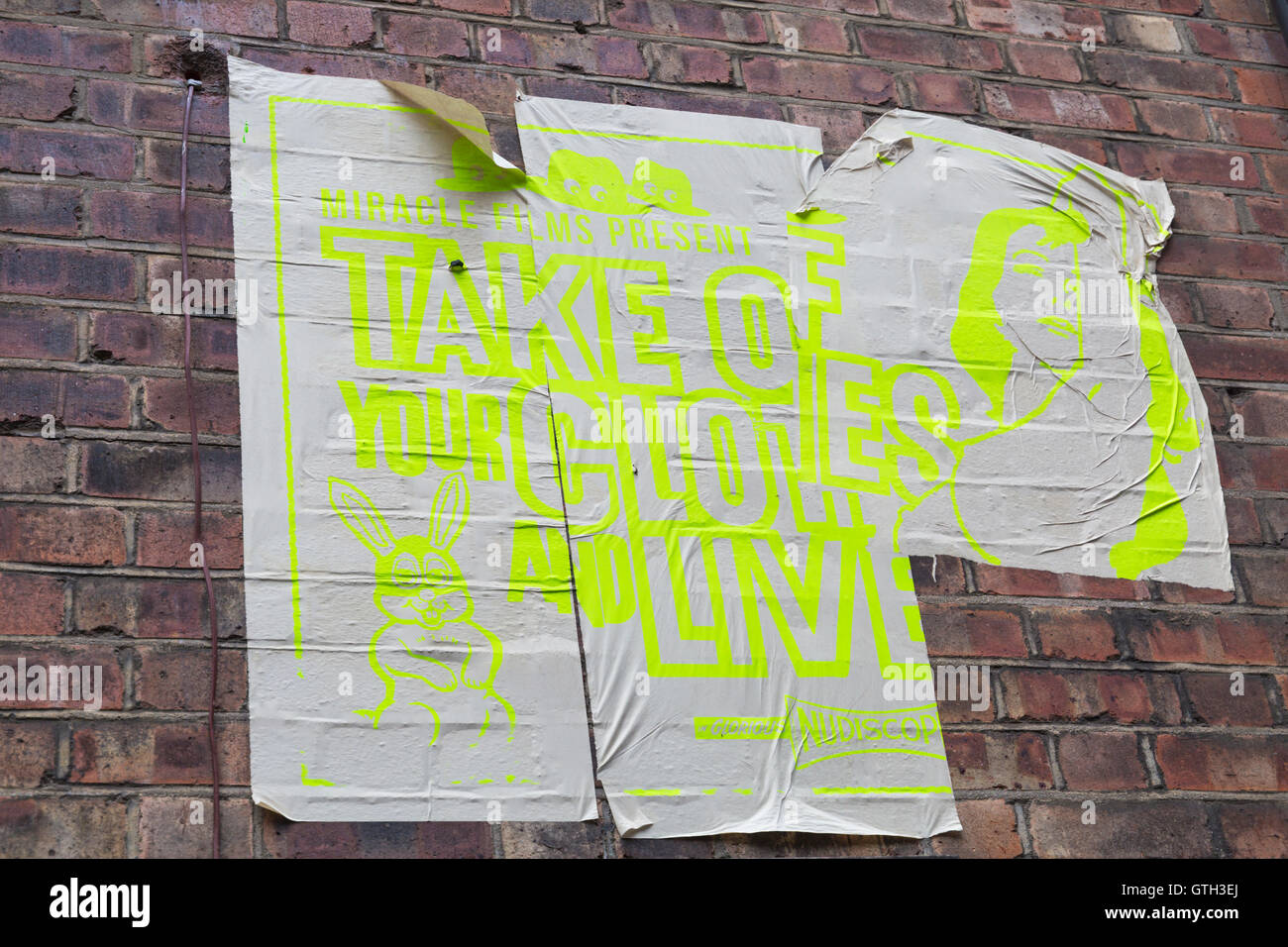 Miracle Films present Take off your clothes and live torn poster on brick wall at Shoreditch, London in September Stock Photo