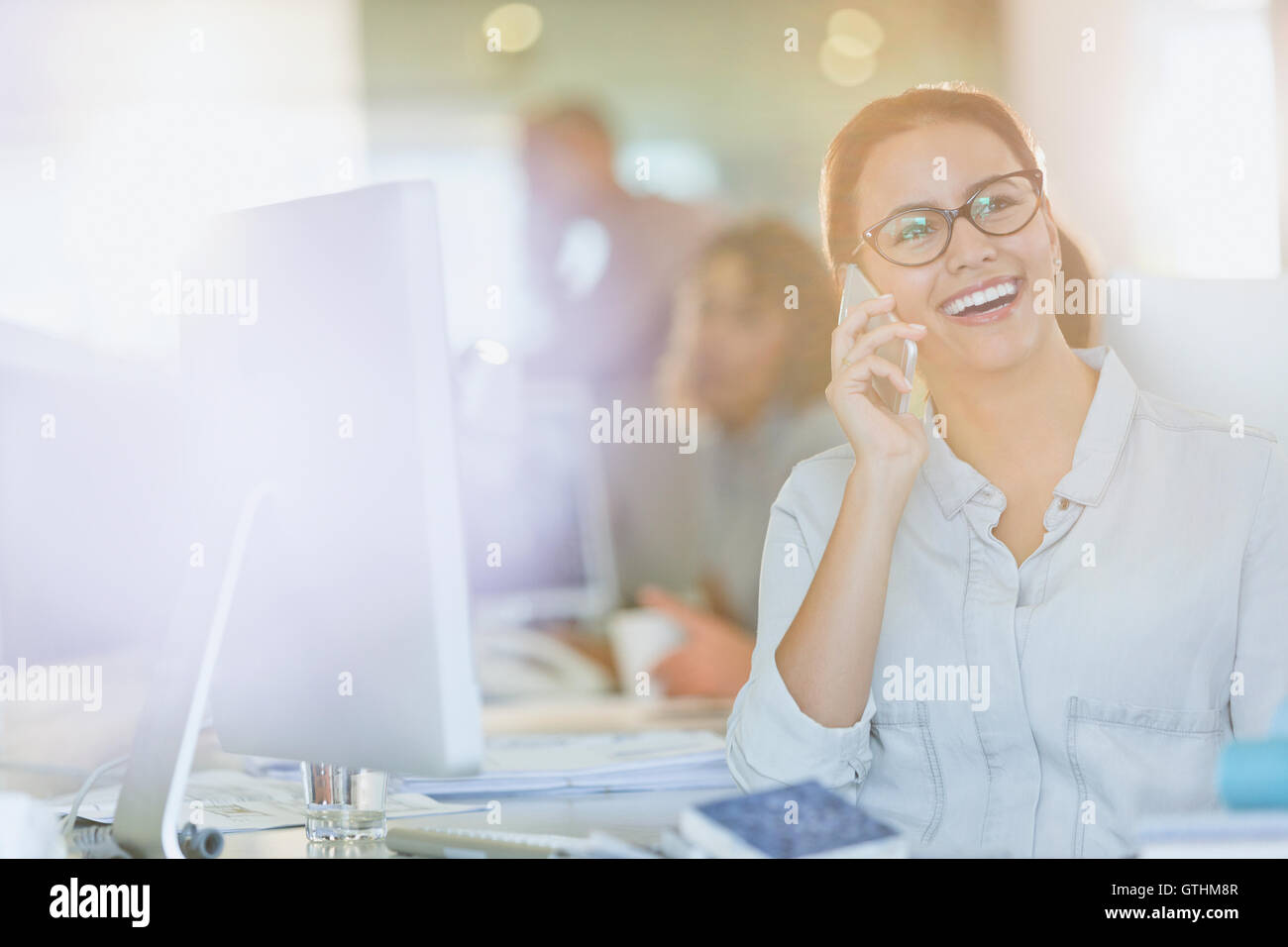 Smiling businesswoman talking on cell phone at computer in office Stock Photo