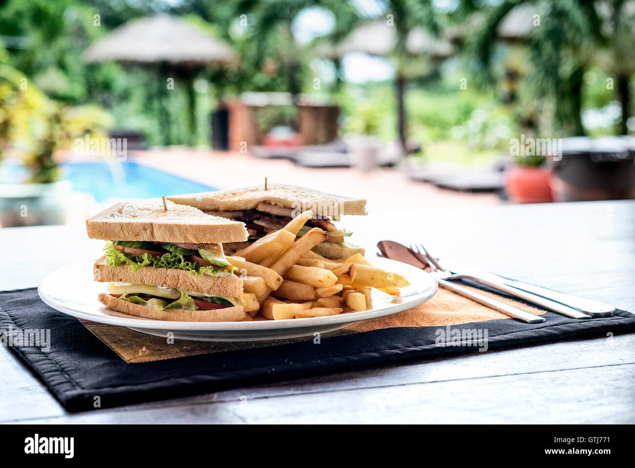 club sandwich snack with french fries on plate in tropical outdoors pool setting Stock Photo