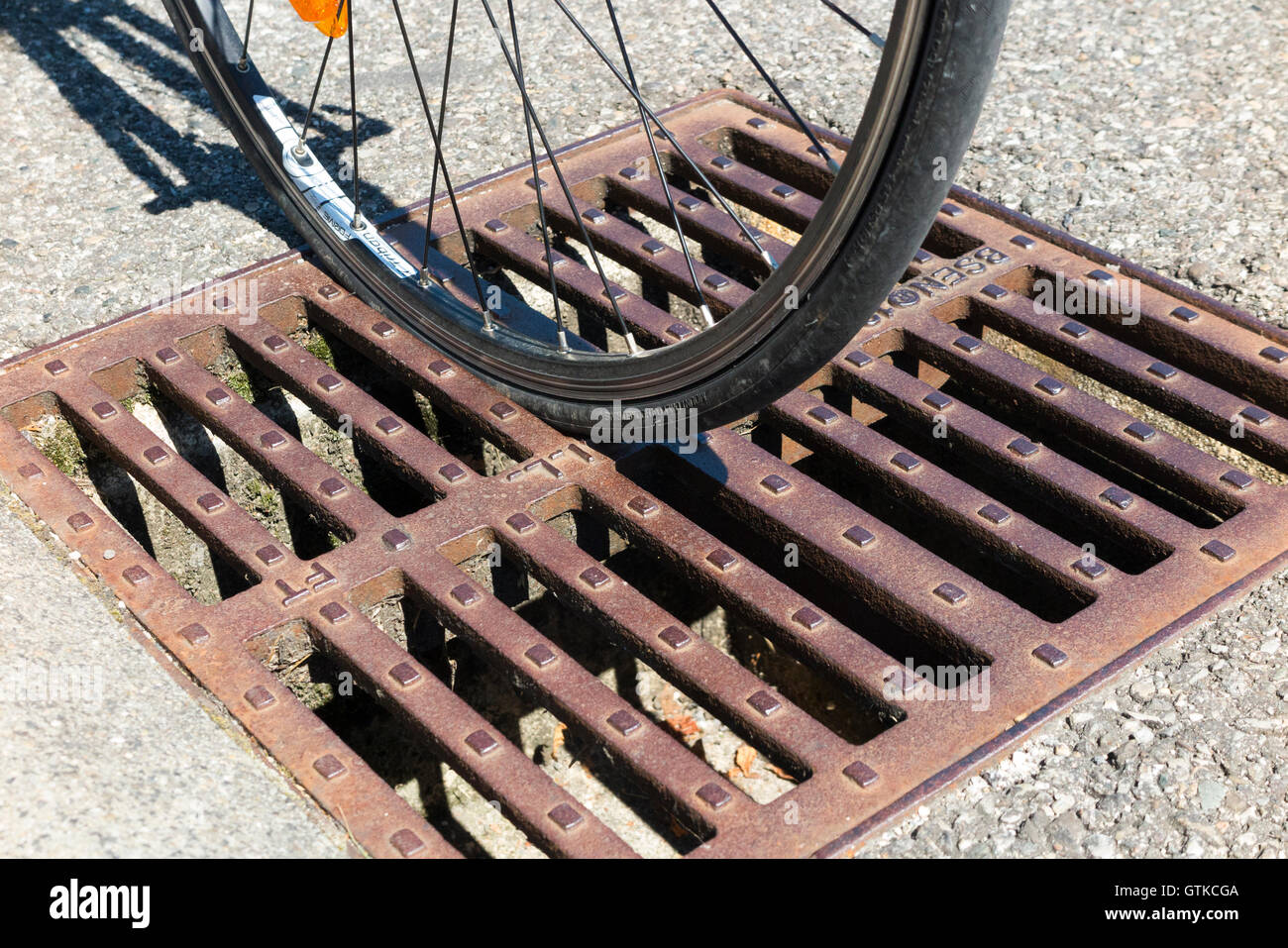 Road bike bicycle cycle wheel which has slotted into a drain grid iron cover placed with slots in the direction of gutter. Stock Photo