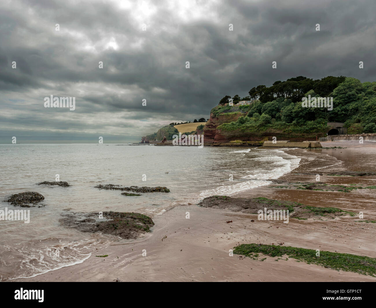 Beautiful landscape depicting storm clouds casting shadows over the South West Coastal Path / beach at Dawlish, Devon. Stock Photo