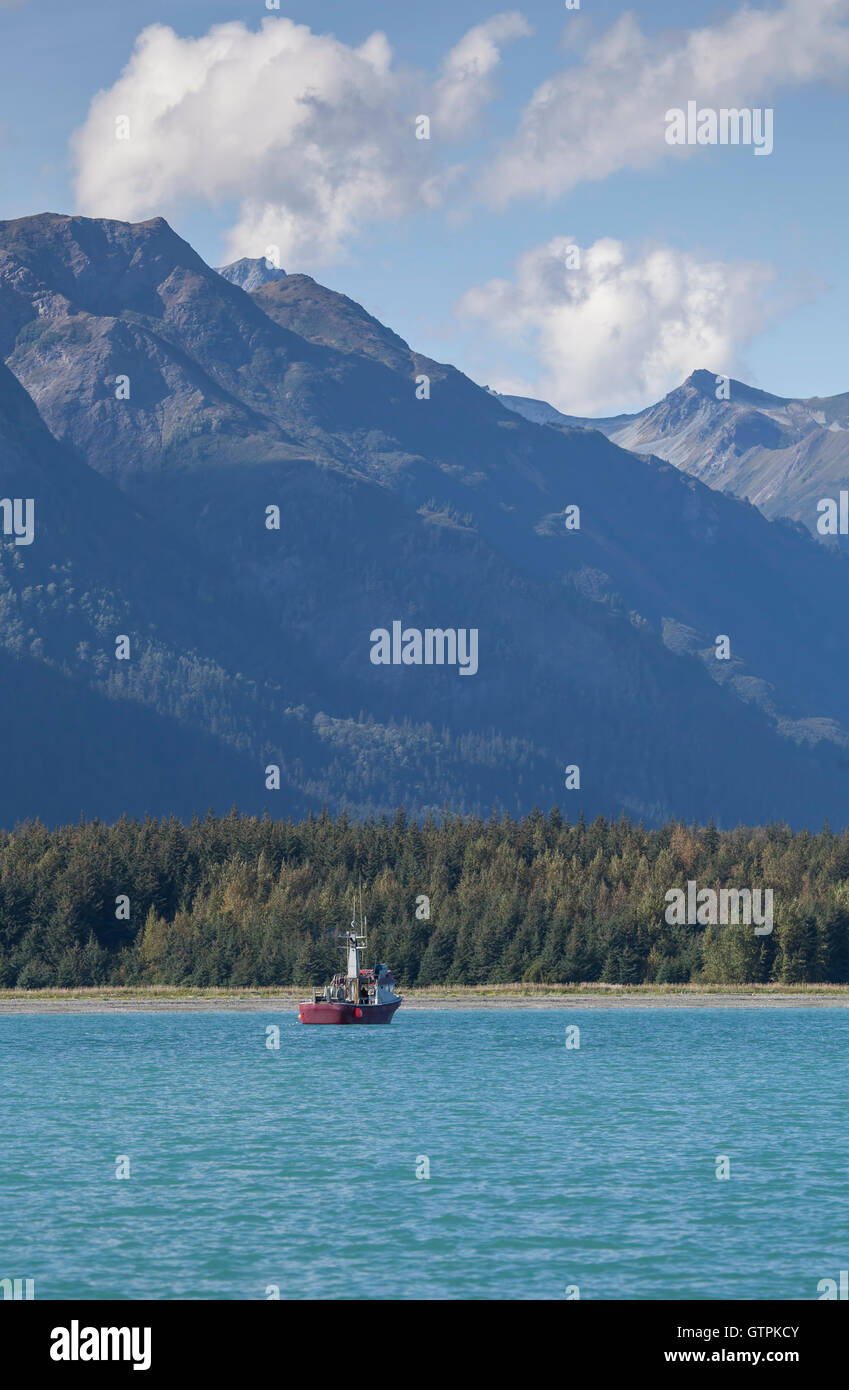 Red commercial fishing boat near Glacier Point in Southeast Alaska in summer with mountains and clouds. Stock Photo