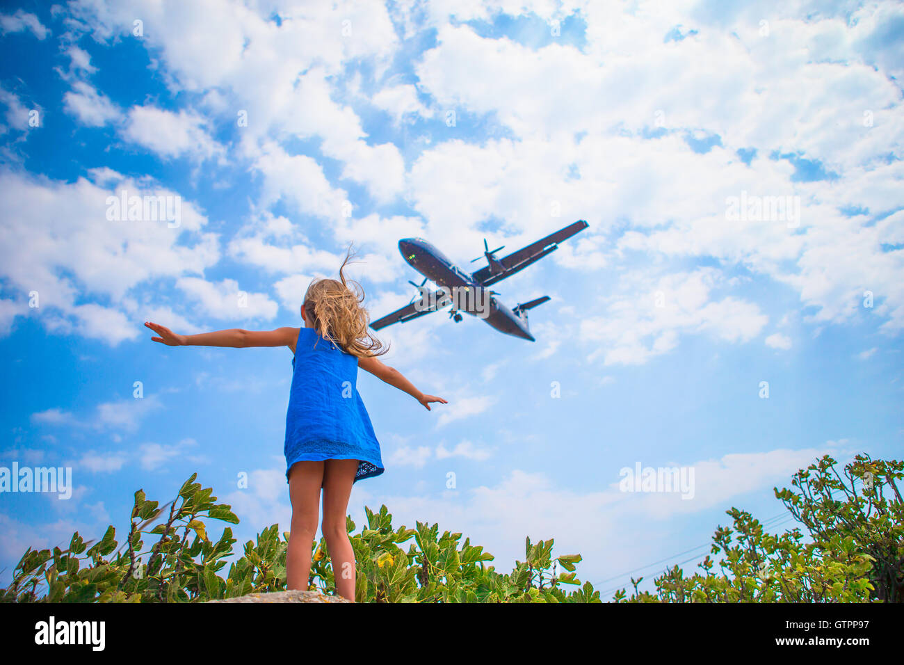 Adorable little child girl looking to the sky and flying plane directly ...