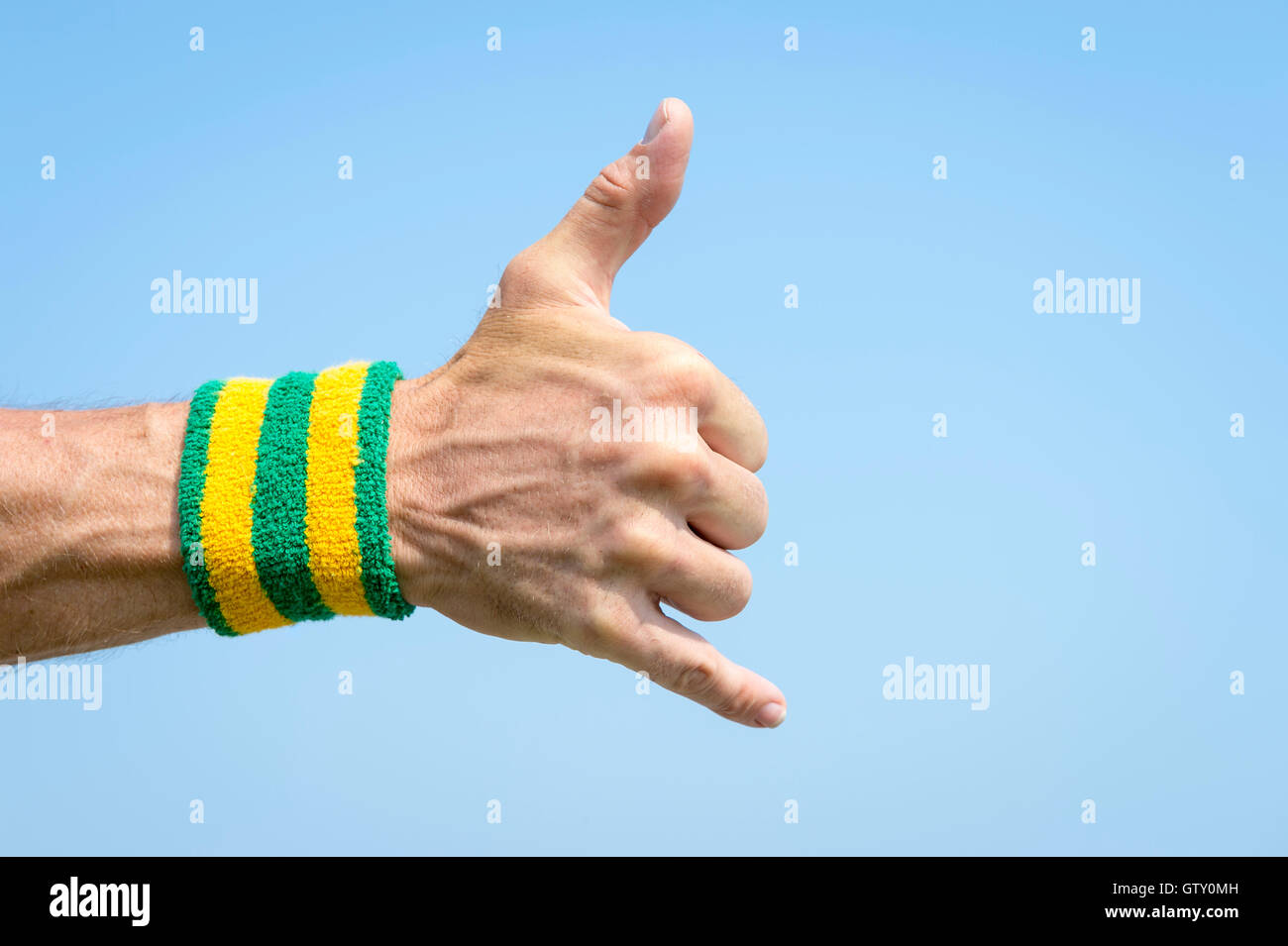 Athlete hand with yellow and green Brazil colors wristband giving a classic  shaka surfer sign against blue sky Stock Photo - Alamy