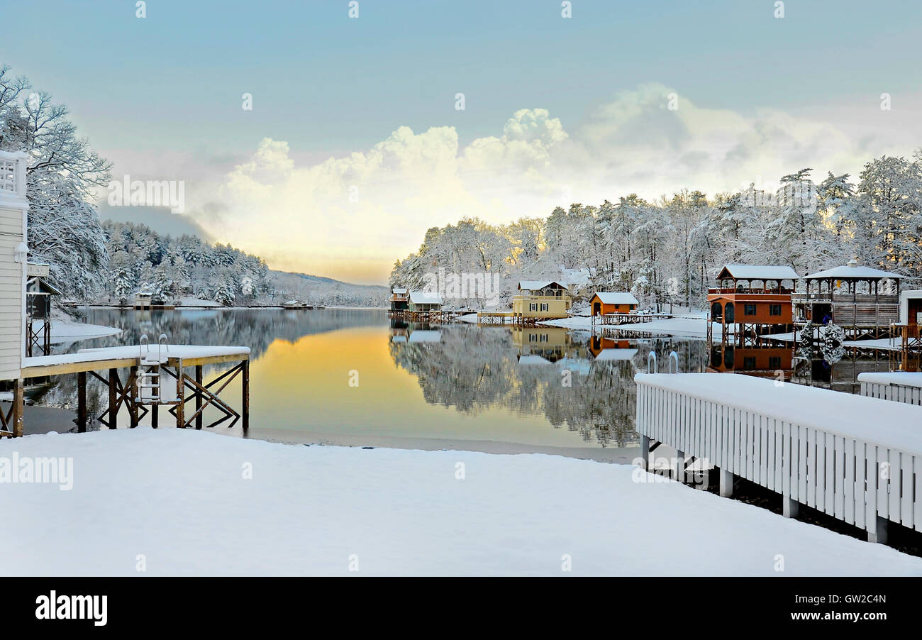 A beautiful wintry early morning lake landscape with homes, snow, lake, mountains, and reflections. Stock Photo