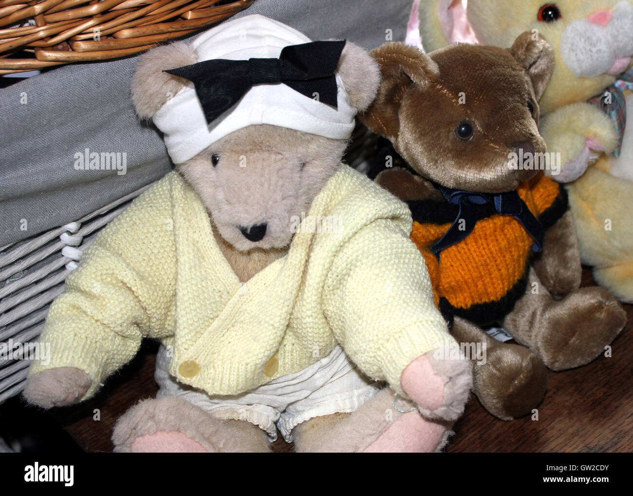 Two toy teddy bears and a rabbit sit together in front of a wicker ...