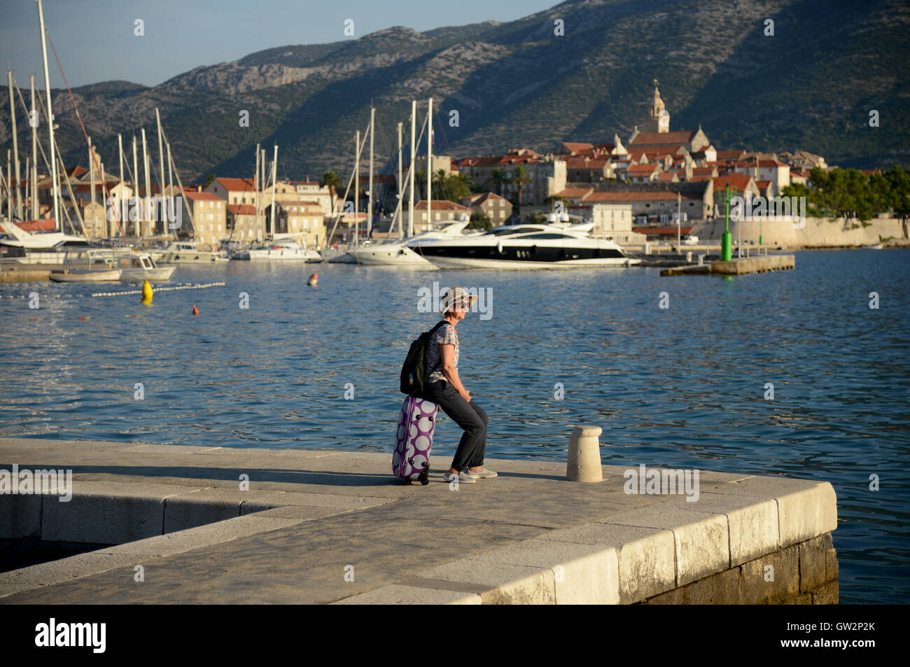 A holidaymaker waits on the quayside for a ferry at Korcula harbour, Croatia. Stock Photo