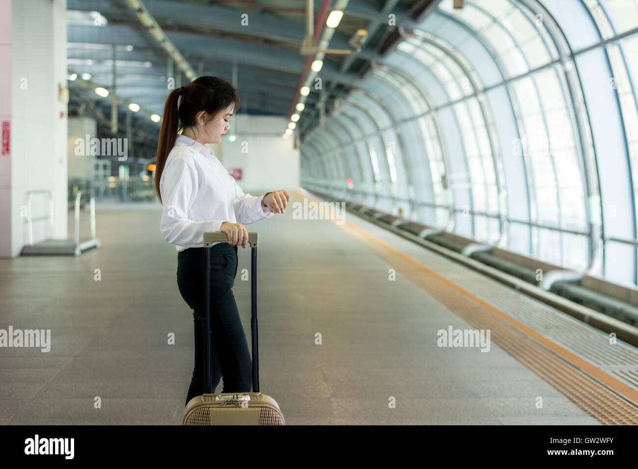 Business travel concept - Young Asian business woman looking in her watch while waiting high speed train at station.Train delay. Stock Photo