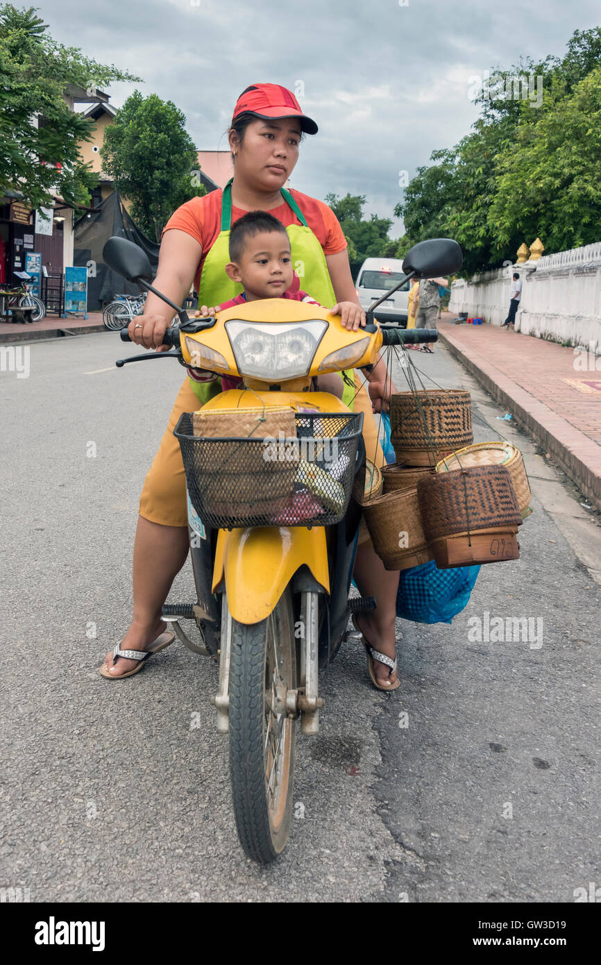 Boy and mom on motorcycle with alms-giving baskets, Wat Sene, Sisavang Vong Road, Luang Prabang, Laos Stock Photo