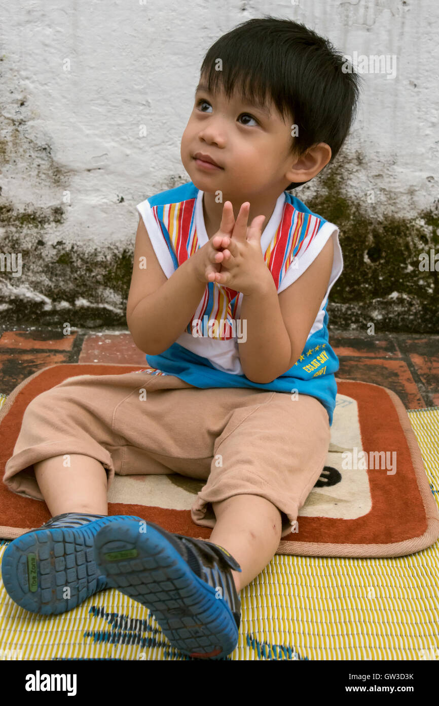 Small boy with hands in attempted namaste position looking up at monk, Wat Sene, Luang Prabang, Laos Stock Photo