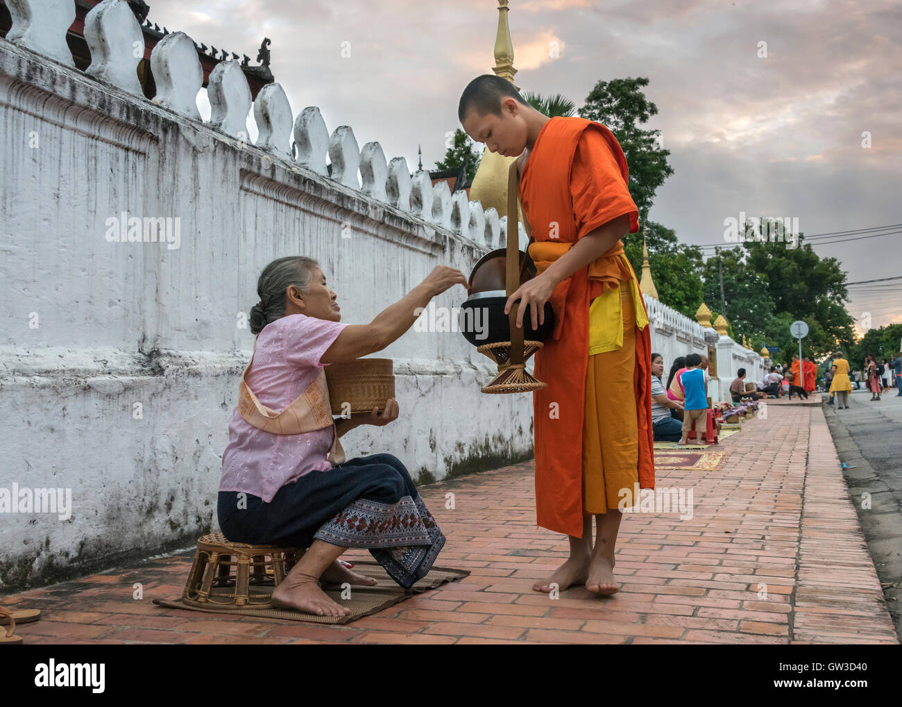 Buddhist monk receiving alms at sunrise, Wat Sene, Sisavang Vong Road, Luang Prabang, Laos Stock Photo