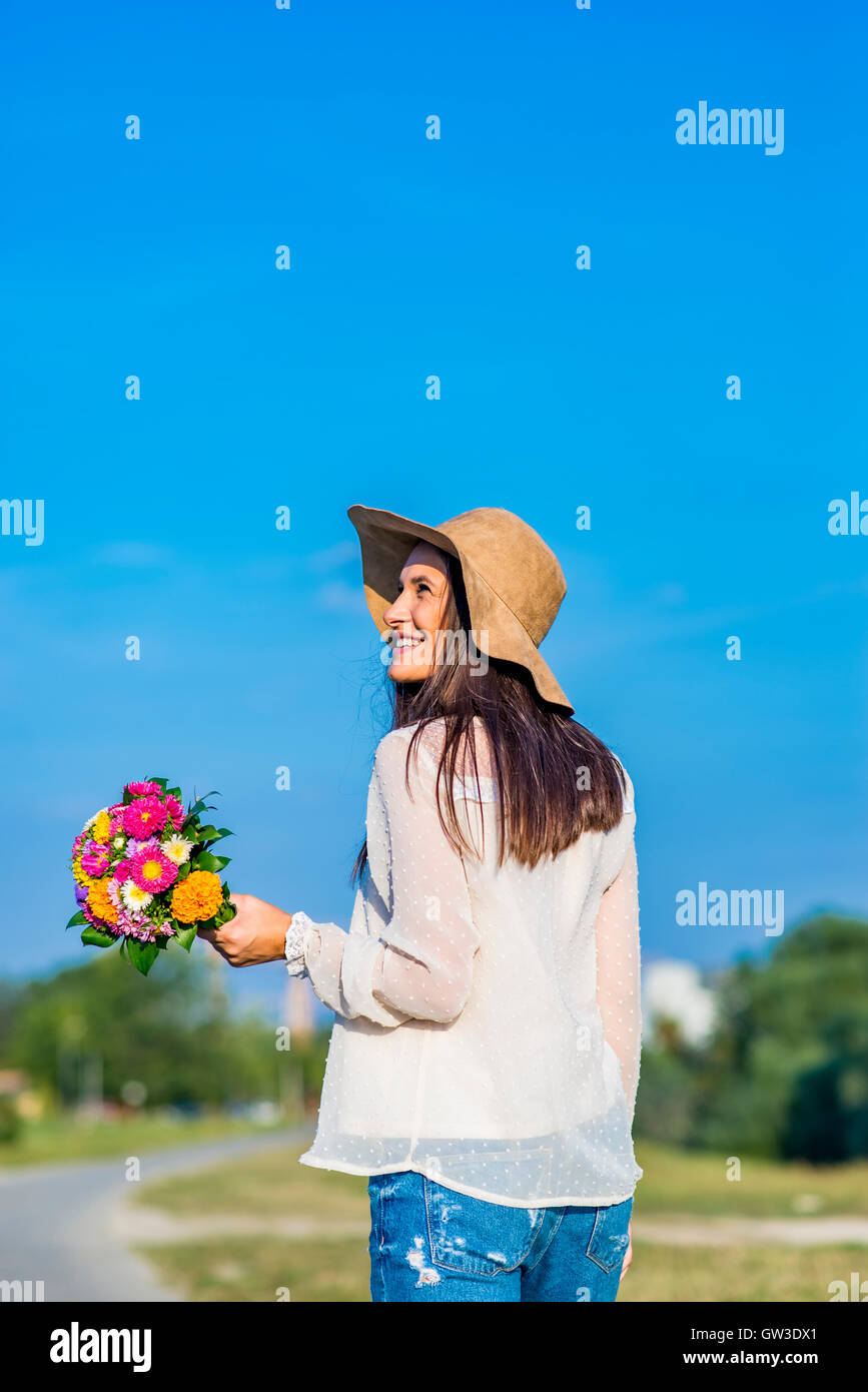 Young woman with a hat and flowers posing outdoors Stock Photo