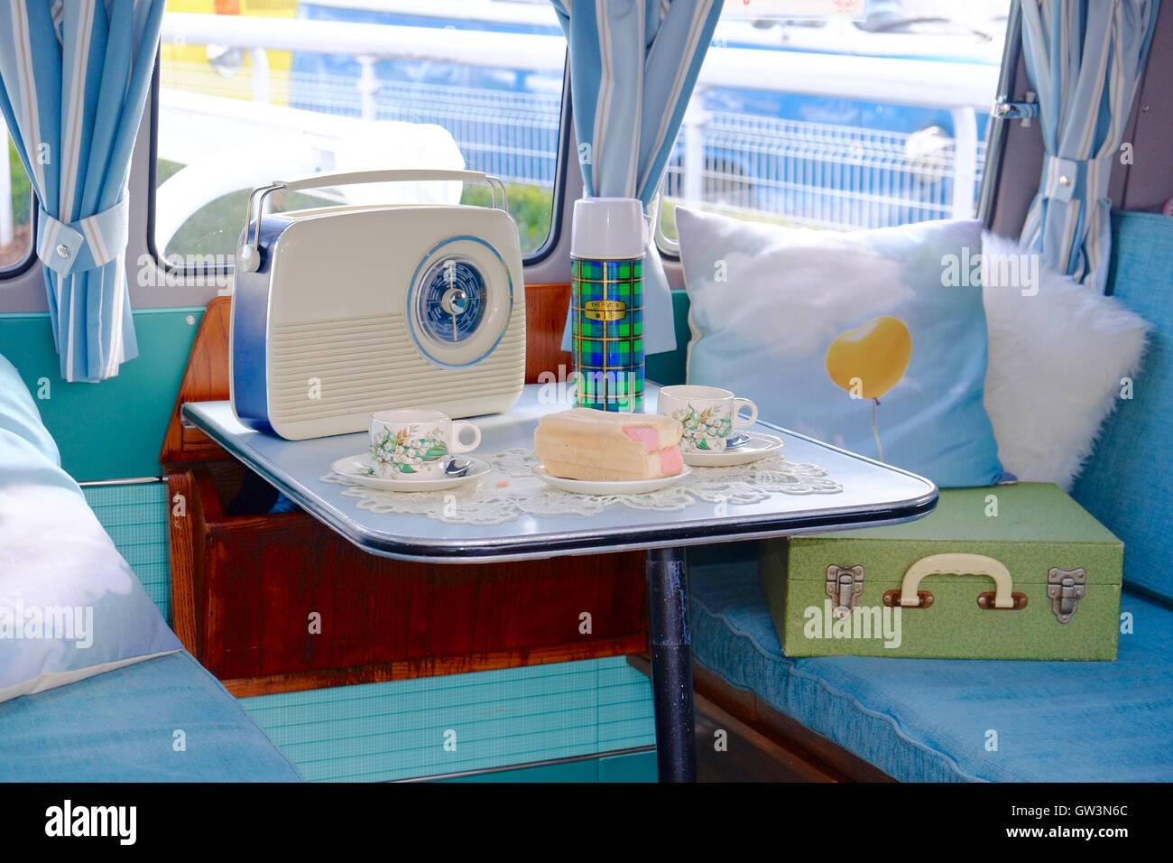 VW Camper van interior, with table set for afternoon tea, with batten-burg cake, thermos flask and retro radio. Stock Photo