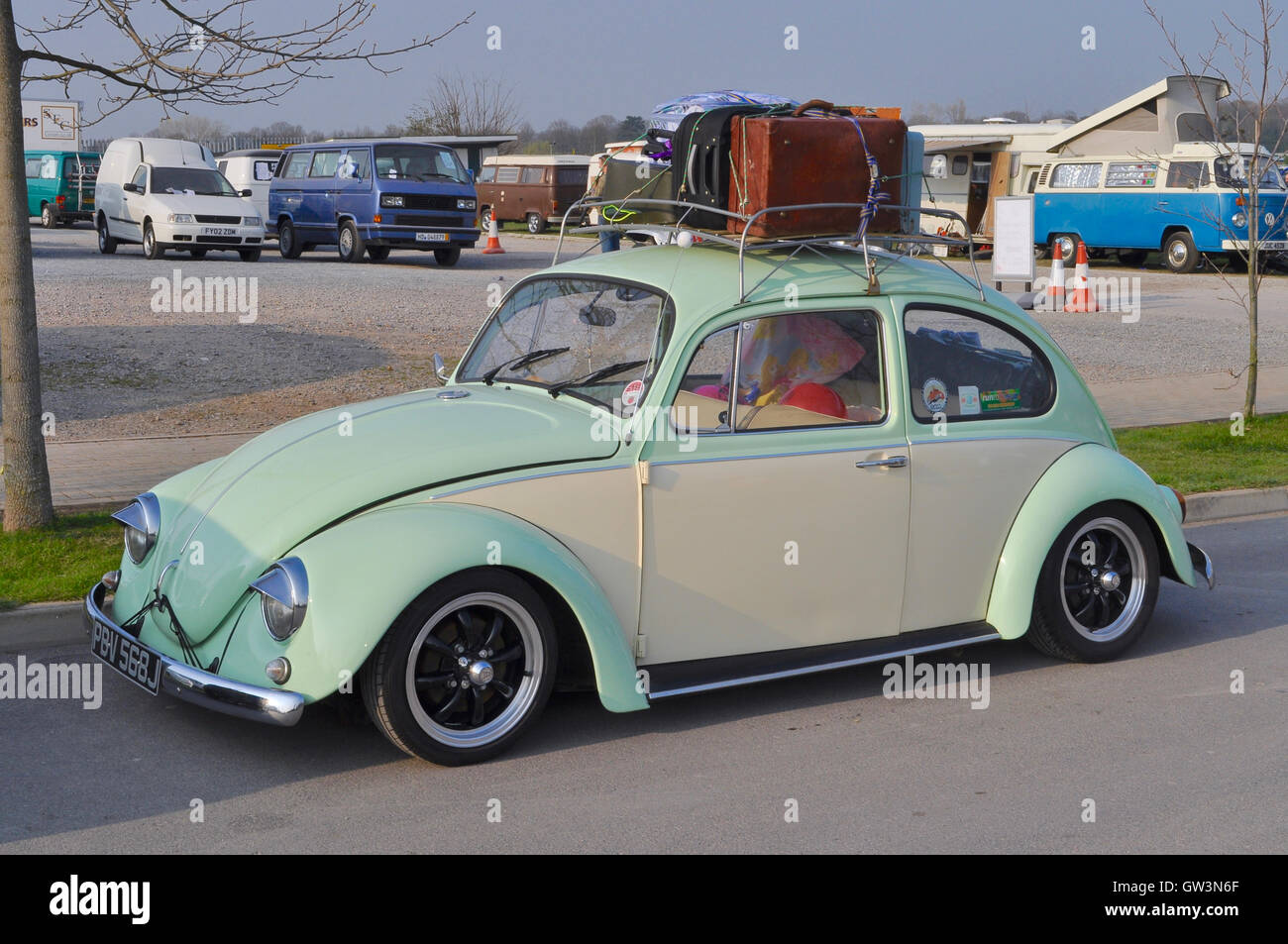 A Classic VW Beetle with luggage rack, parked with classic VW camper vans in the background. Stock Photo