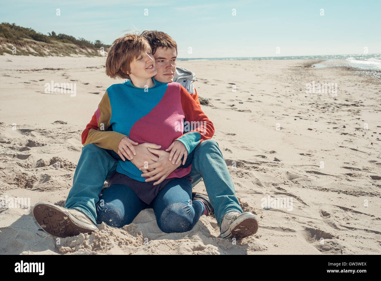 Young man embracing a woman sitting on the beach Stock Photo - Alamy