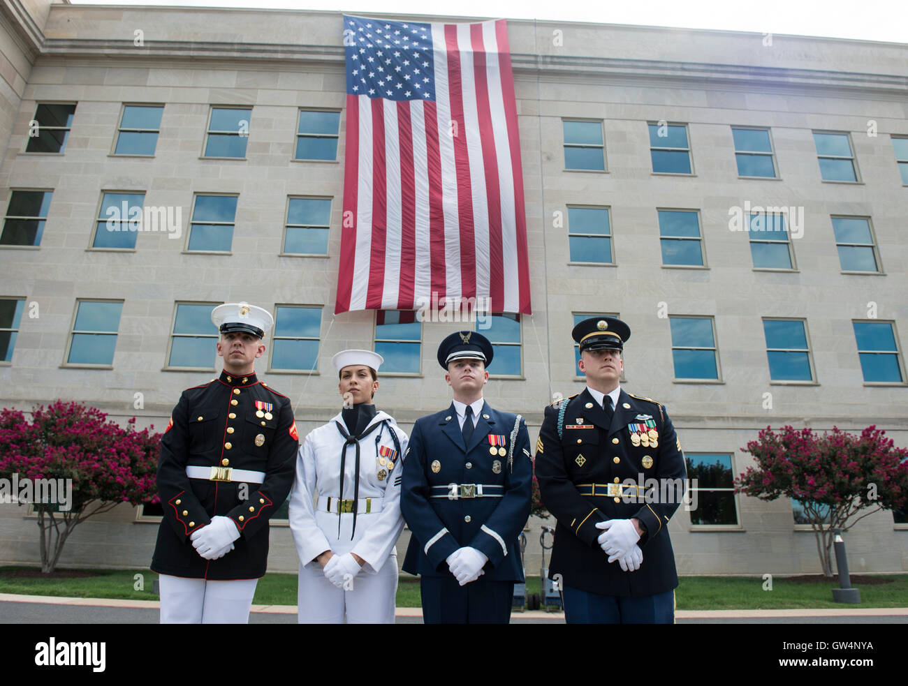 U.S Service members stand in front of a flag hanging from the Pentagon where the aircraft plowed into the building 15-years-ago during a remembrance ceremony commemorating the 15th anniversary of the 9/11 terrorist attacks at the Pentagon September 11, 2016 in Arlington, Virginia. Stock Photo