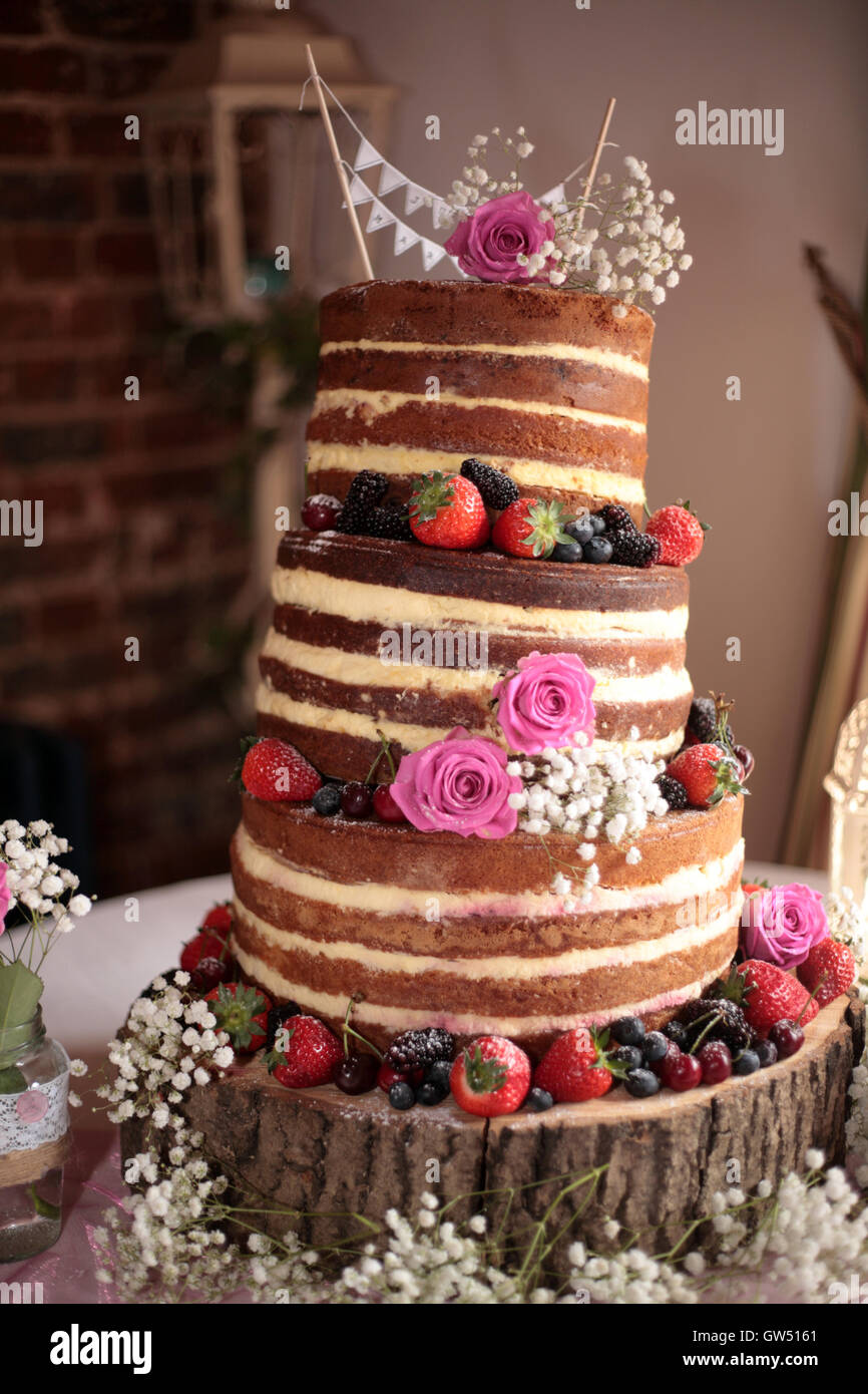 A topsy turvy wedding cake set upon a log with fresh berries. Stock Photo