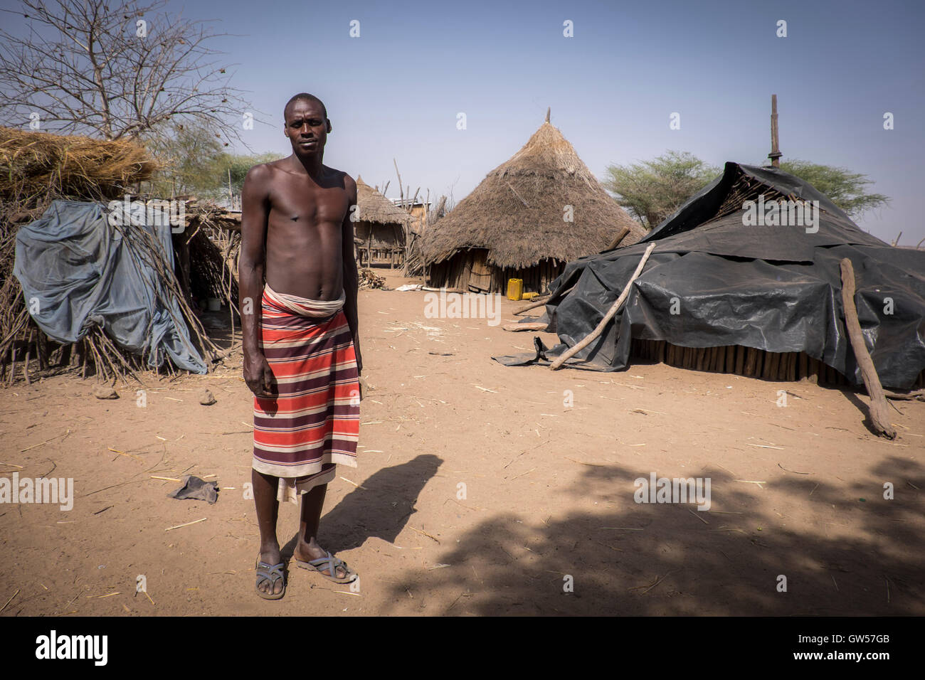 Tall male of the Karo tribe in his village in the Omo Valley of Ethiopia with thatched huts in the background Stock Photo