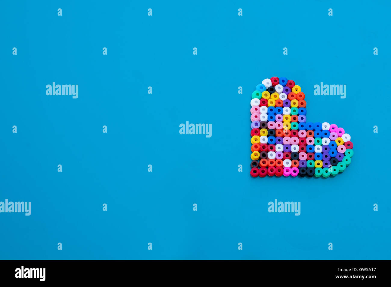 Tilted colorful heart on blue background. Crafted out of beads. Fun love hipster concept. Space for text. Stock Photo