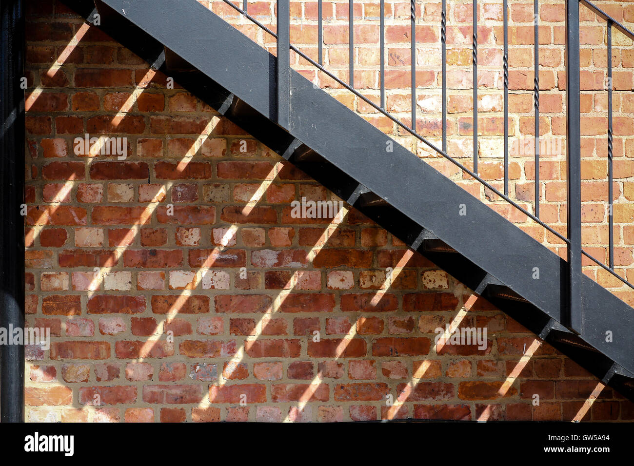 Shadows cast by an iron fire escape against a red brick wall Stock