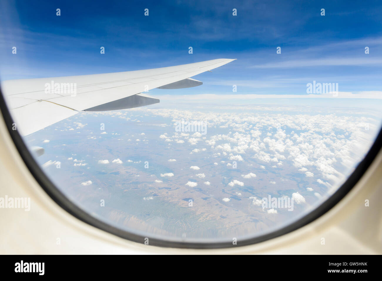Land clouds and sky seen through window of aircraft cabin. Stock Photo