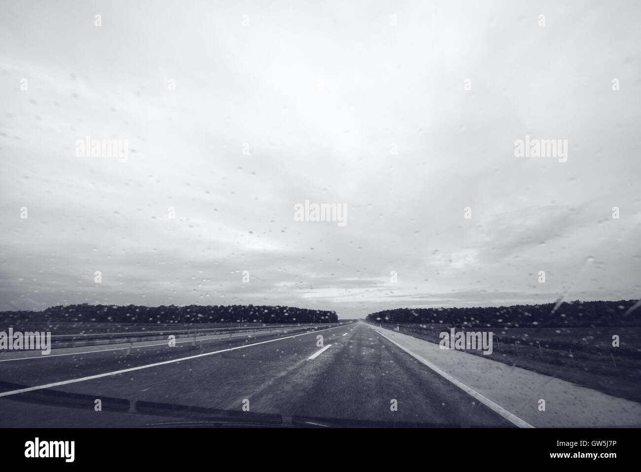 Raindrops on car windshield glass, monochromatic image of open highway through vehicle windscreen on a rainy day Stock Photo