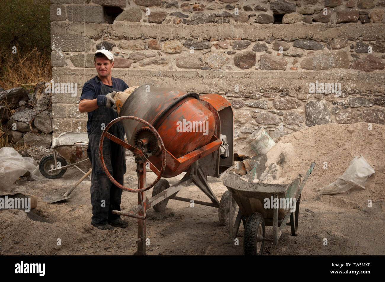 Albanian worker mixes cement for a construction job repairing a wall in Greece Stock Photo
