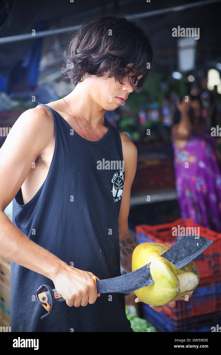 HILO, HAWAII - JUL 13, 2013: An unidentified young man cuts the husk of a coconut at the Hilo farmers market on July 13, 2013. Stock Photo