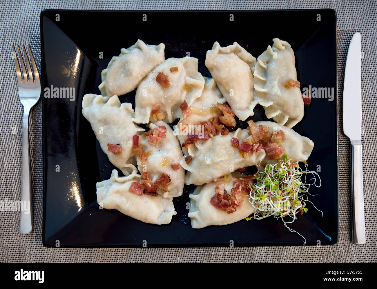 Polish Pierogi stuffed dumplings served in traditional restaurant on a black plate and decorated with ham and green sprouts Stock Photo