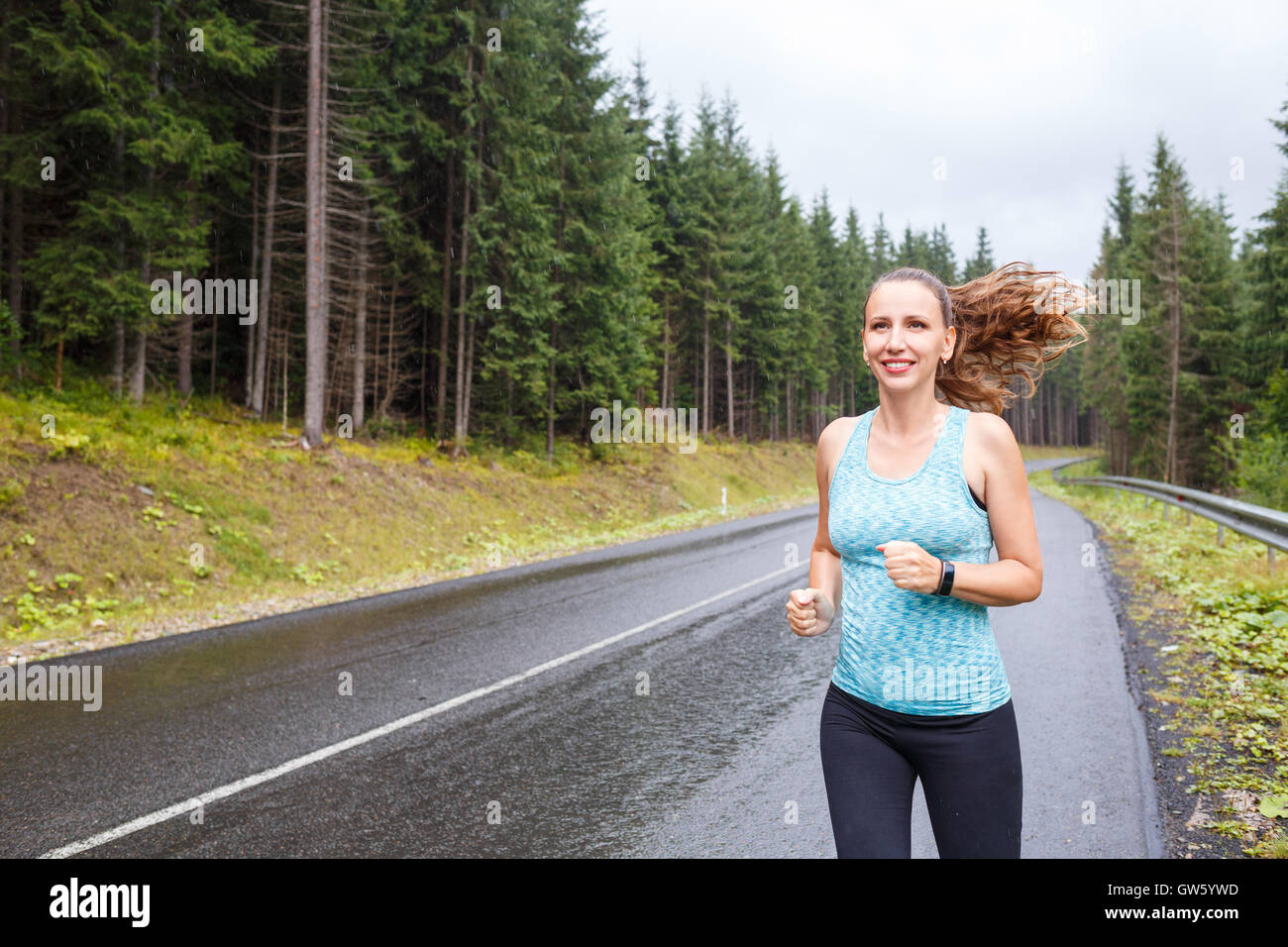 Young slim woman jogging on mountain road at rainy morning Stock Photo