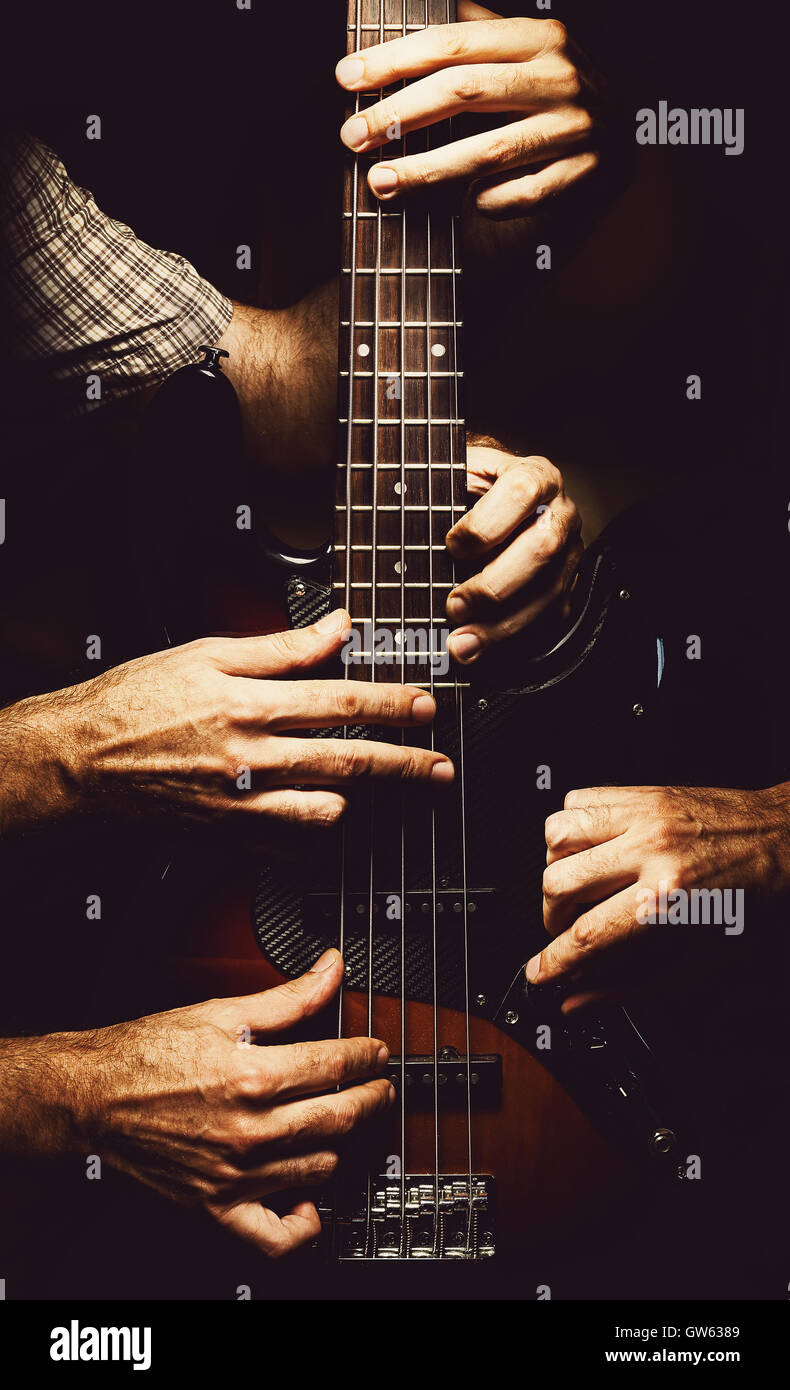 Conceptual composition about playing a modern jazz bass guitar, multiple hands on an instrument. Stock Photo