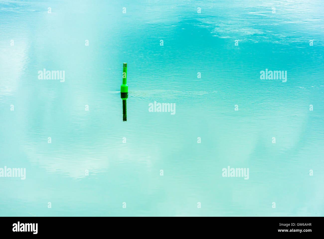 Green navigational buoy in flowing river water and sky reflecting in the calm water. Stock Photo