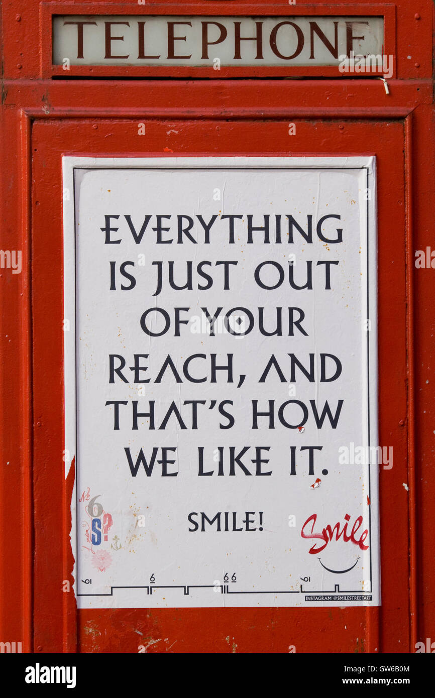 Telephone box with a notice saying notice saying 'Everything is just out of our reach and thats how we like it' Smile on it Stock Photo