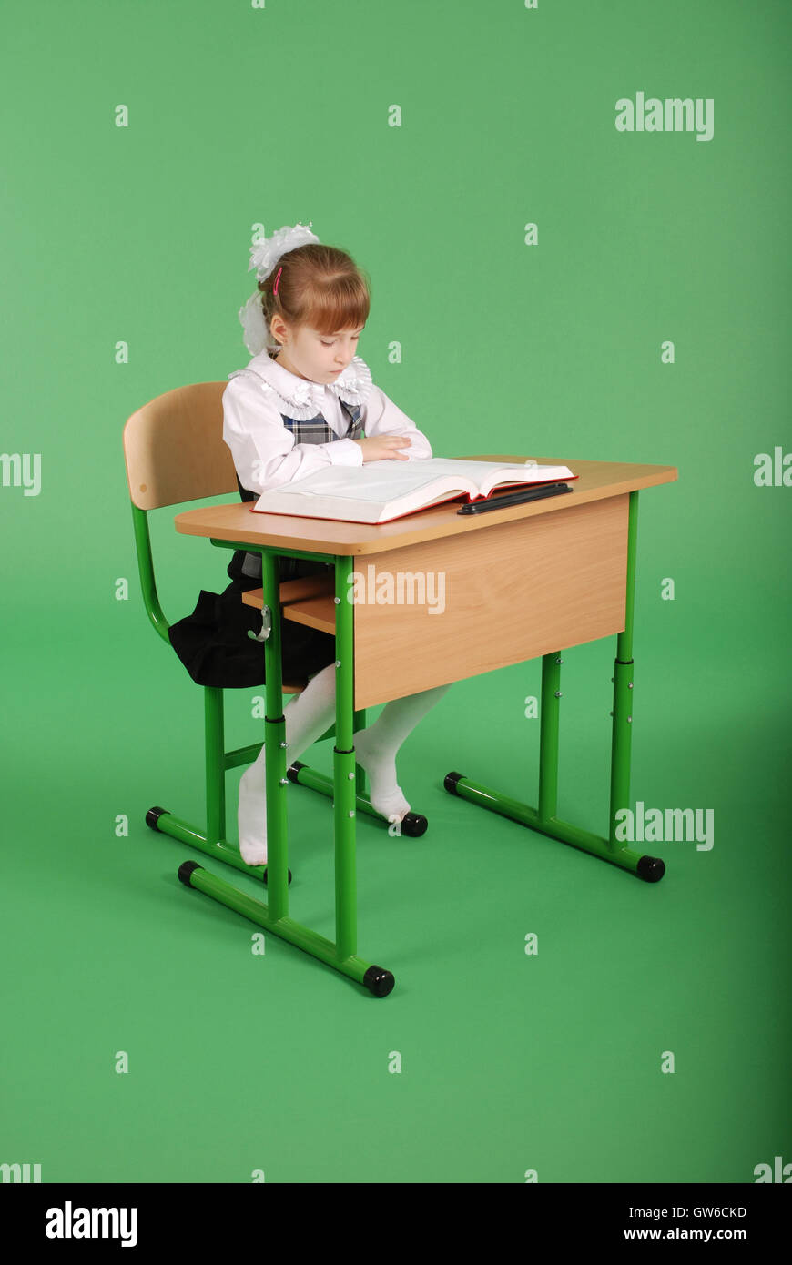 Girl in a school uniform sitting at a desk and reading a book isolated ...