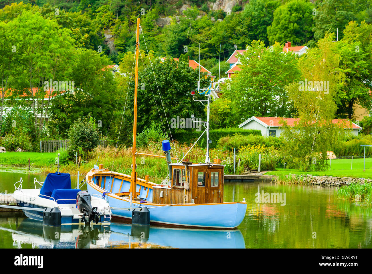 Kungalv, Sweden - September 8, 2016: Traveling in Sweden, blue fishing boat moored riverside with trees and homes in the backgro Stock Photo