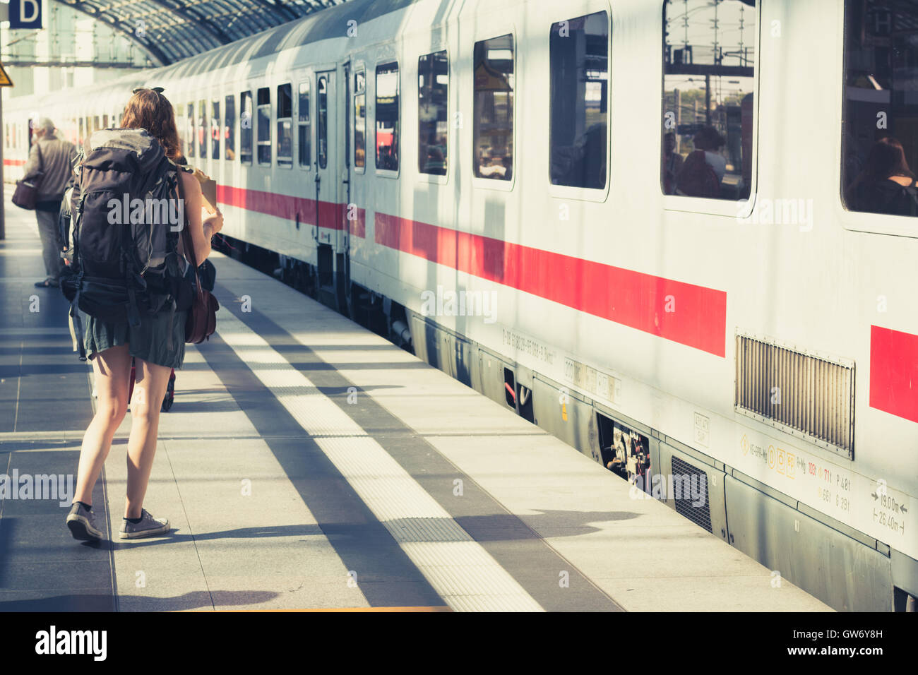 Girl with backpack from behind standing at platform before entering train. Stock Photo