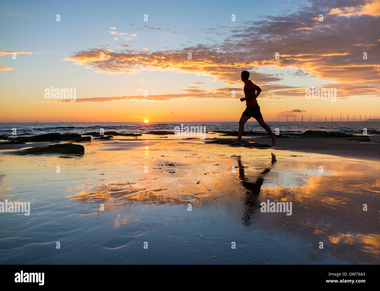 Seaton Carew, north east England, UK. 12th Sep, 2016. Weather: A jogger on Seaton Carew beach as the sky explodes with colour at sunrise on a glorious Monday morning on the north east coast. The Met office predicts that in the early part of the week the UK may see the hottest September day for more than 40 years. Credit:  Alan Dawson News/Alamy Live News Stock Photo