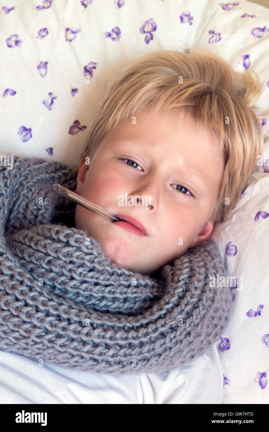 Sick little boy holding thermometer laying in bed with sad face - healthcare and medicine concept Stock Photo