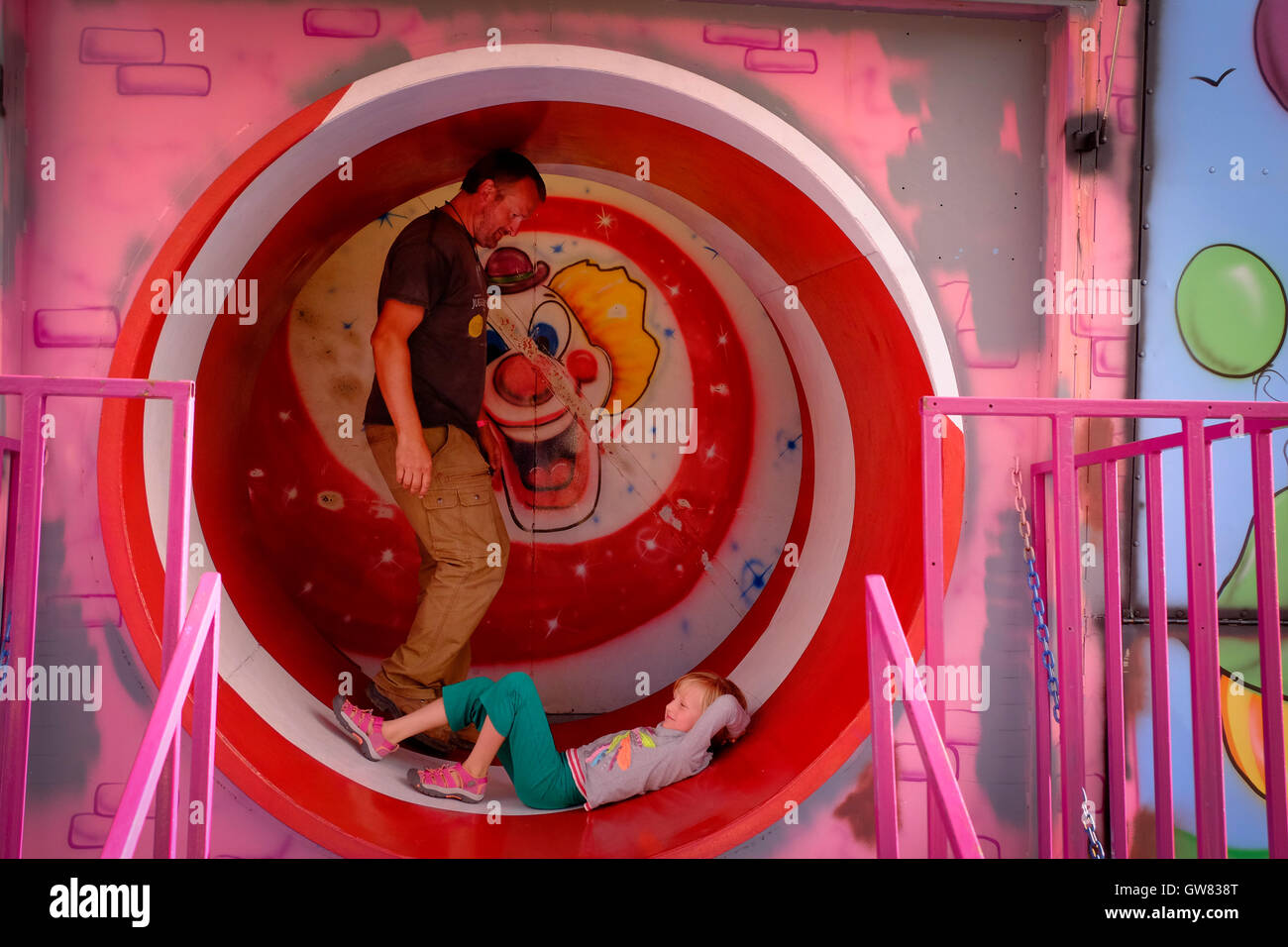 Father and daughter at play in the final room of a fun house with a moving tubular exit Stock Photo