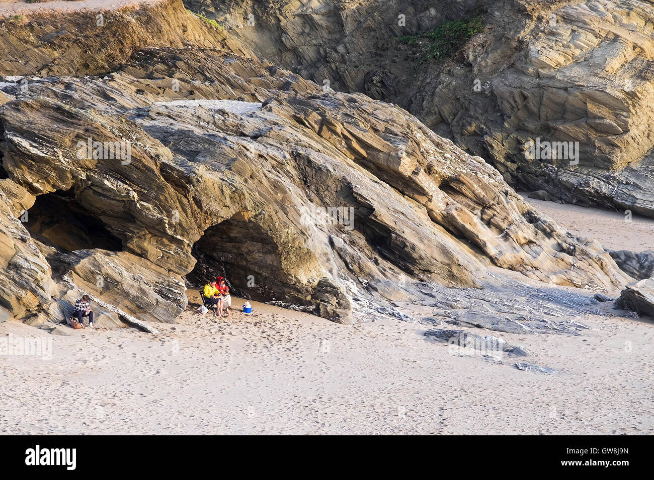 Two people sit in a cave on the beach at Little Fistral in Newquay, Cornwall. Stock Photo