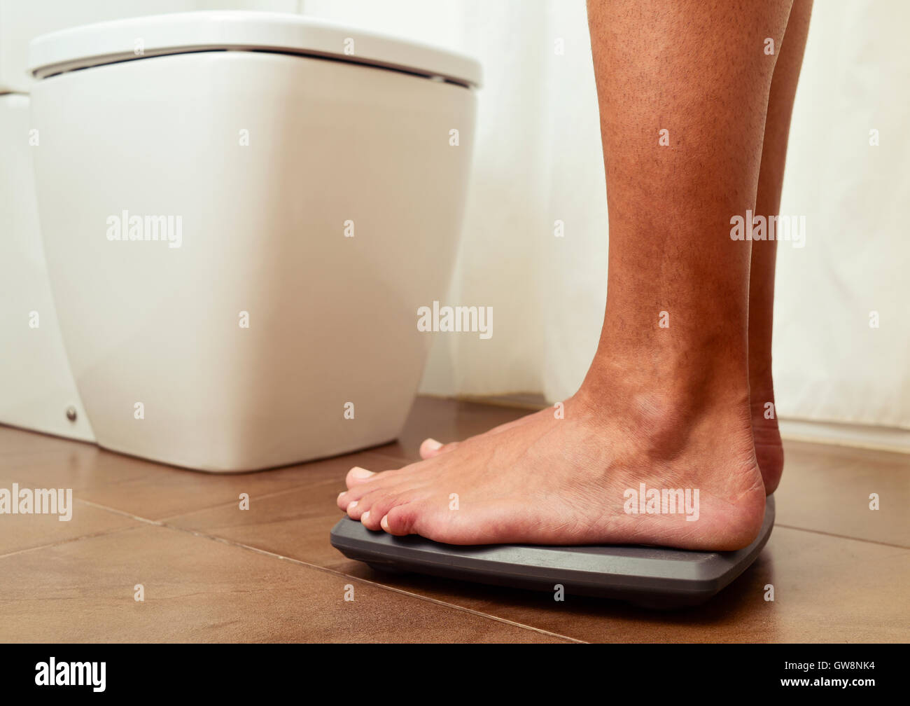 closeup of a young man standing on a scale, to check out his weight, into the bathroom Stock Photo