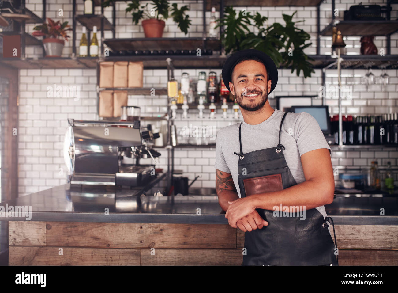 Proud coffee shop owner at the counter. Coffee shop worker in apron and hat leaning to counter. Stock Photo