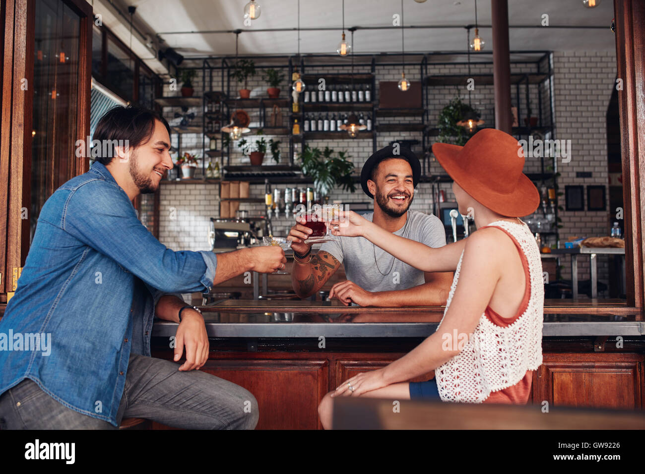 Young friends at cafe toasting drinks while sitting at a table. Three young people, two men and a woman meeting in a coffee shop Stock Photo