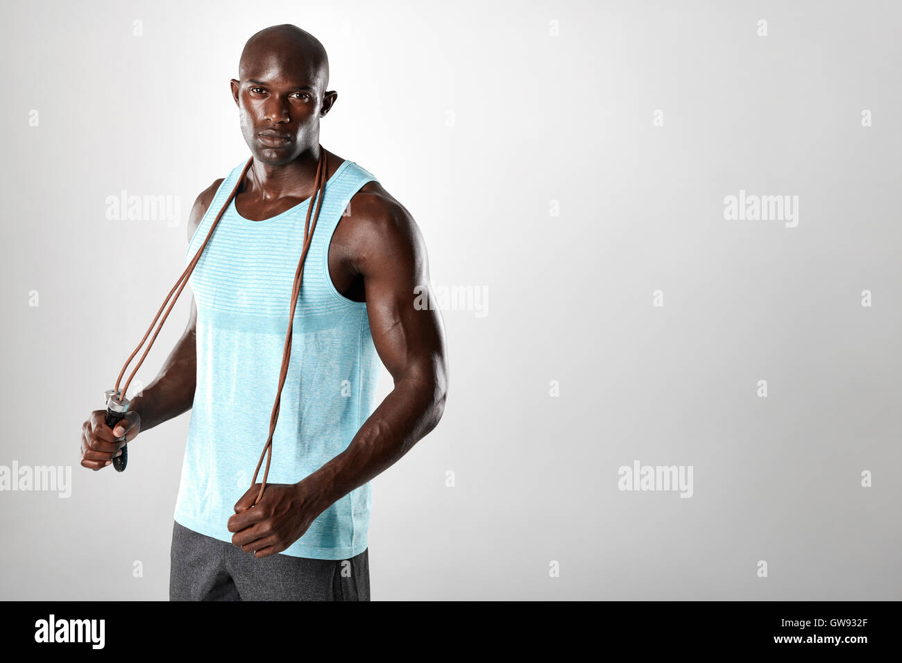 Fit and muscular man with jumping rope on grey background. African male model looking at camera with skipping rope. Stock Photo