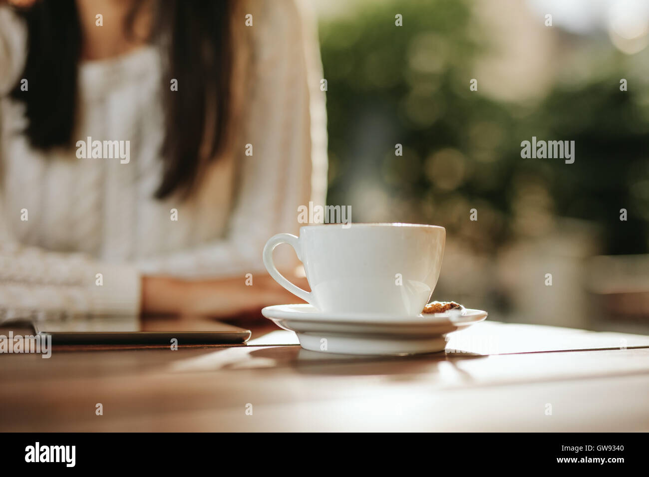 Close up shot of cup of coffee and digital tablet on cafe table with woman. Stock Photo