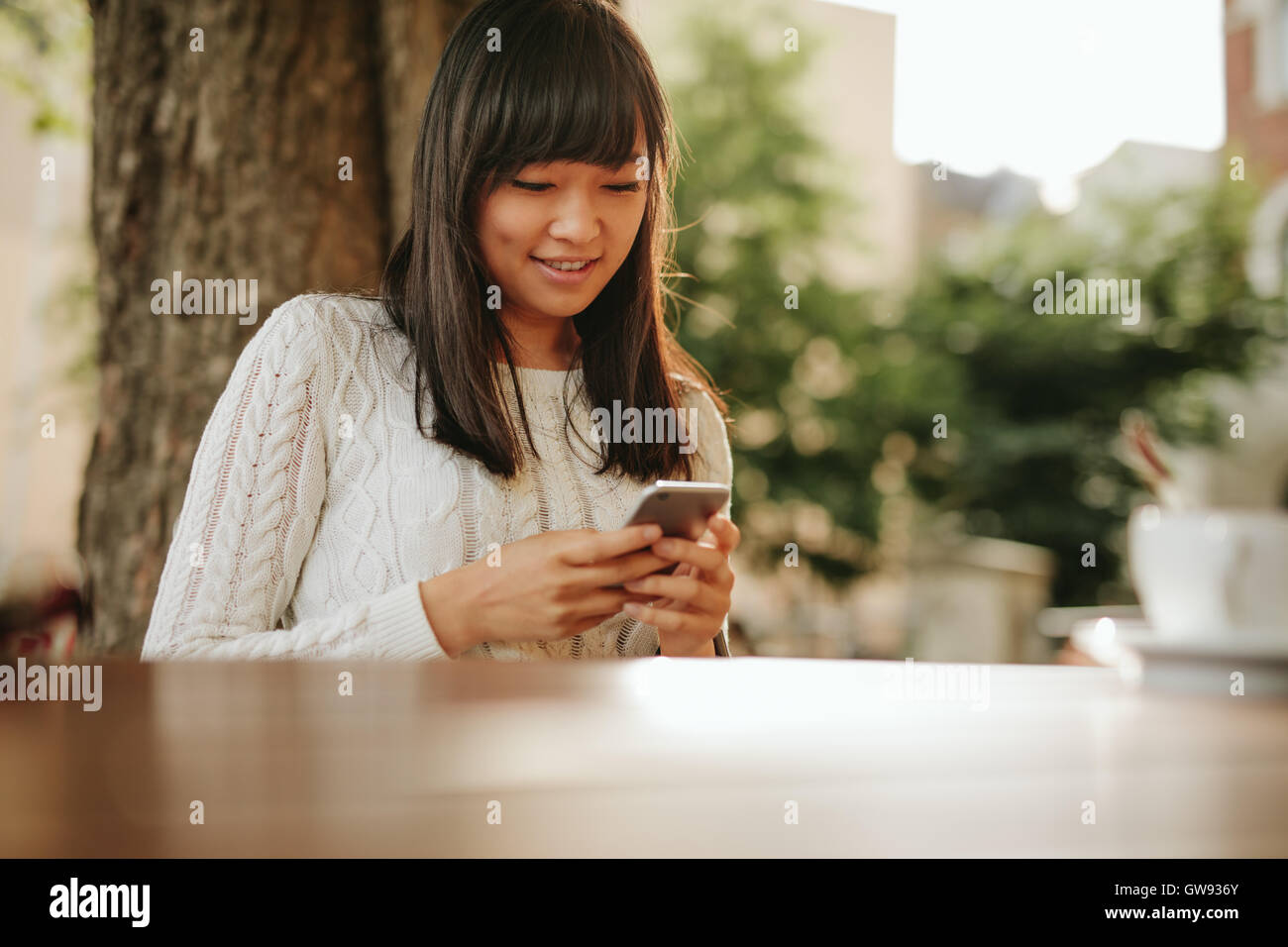 Shot of young asian female reading a text message on her smart phone. Woman using smart phone in a outdoor cafe. Stock Photo